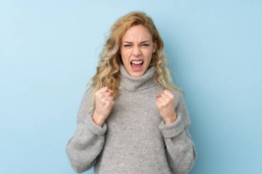 Mavi arka planda izole edilmiş süveter giyen genç sarışın kadın kötü bir durum yüzünden hayal kırıklığına uğradı.