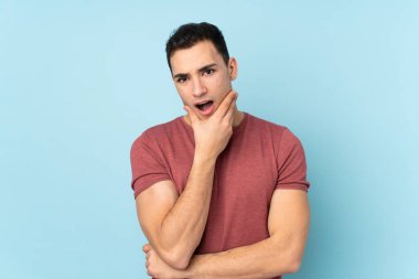 Mavi arka planda izole edilmiş beyaz, yakışıklı genç adam sağa bakarken şaşırmış ve şok olmuştu.