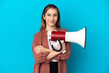 Mavi arka planda izole edilmiş genç beyaz bir kadın elinde bir megafon ve gülümsüyor.