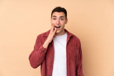 Beyaz tenli yakışıklı adam bej arka planda izole edilmiş, şaşırmış ve şok olmuş bir yüz ifadesi var.