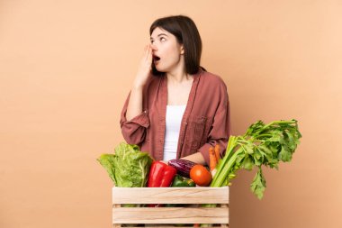 Genç çiftçi kız taze toplanmış sebzelerle bir kutuda esniyor ve ağzını eliyle kocaman açık tutuyor.