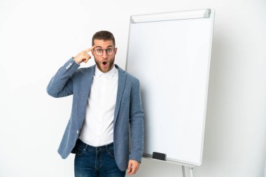Beyaz arka planda izole edilmiş yakışıklı beyaz bir adam beyaz tahtada sunum yapıyor ve çözümün ne olduğunu anlamaya çalışıyor.