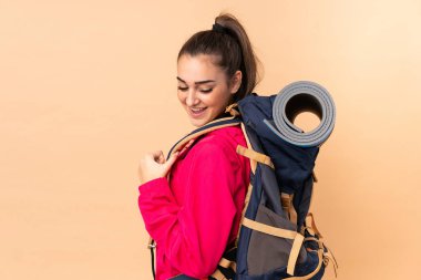 Bej arka planda izole edilmiş büyük bir sırt çantalı genç dağcı kız.