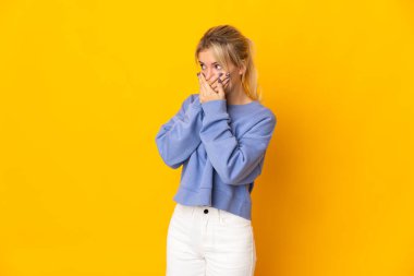 Sarı arka planda izole edilmiş genç bir Rus kadın ağzını kapatıyor ve yan tarafa bakıyor.