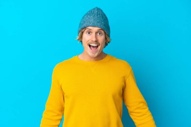 Yakışıklı sarışın adam, mavi arka planda mahsur kalmış, şaşırmış bir yüz ifadesi var.