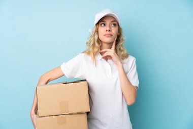 Genç teslimatçı kadın mavi arka planda izole edilmiş bir fikir düşünüyor.