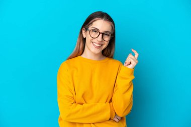 Mavi arka planda izole edilmiş genç beyaz kadın gülüyor.