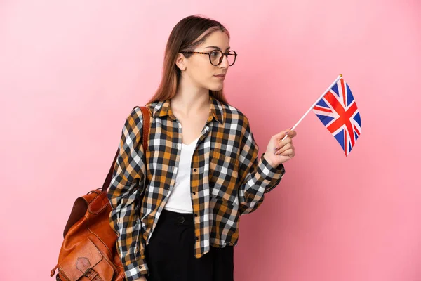 年轻的惊慌失措的女人举着一面英国国旗 与粉色背景隔离 向侧面看去 — 图库照片