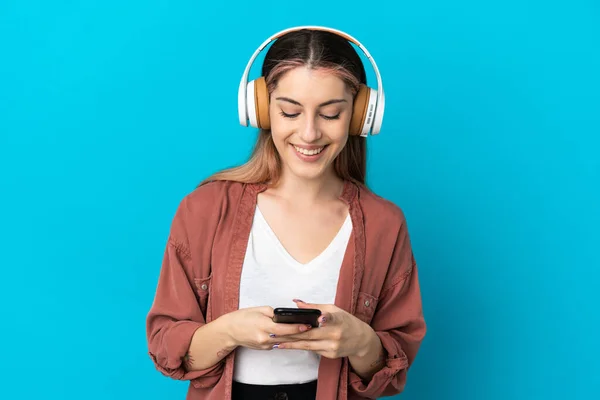 Giovane Donna Caucasica Isolata Sfondo Blu Ascoltando Musica Guardando Cellulare — Foto Stock