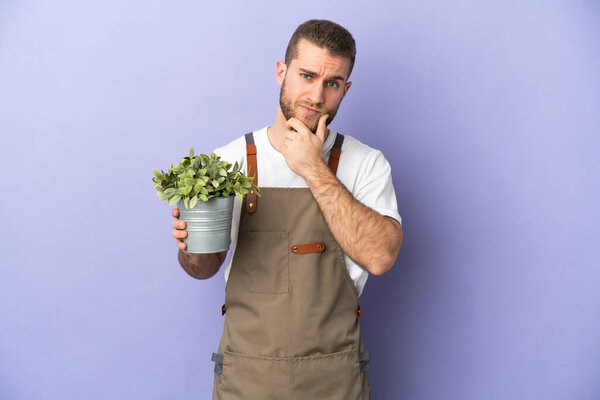 Gardener caucasian man holding a plant isolated on yellow background thinking