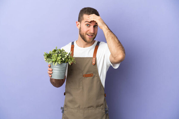 Gardener caucasian man holding a plant isolated on yellow background doing surprise gesture while looking to the side