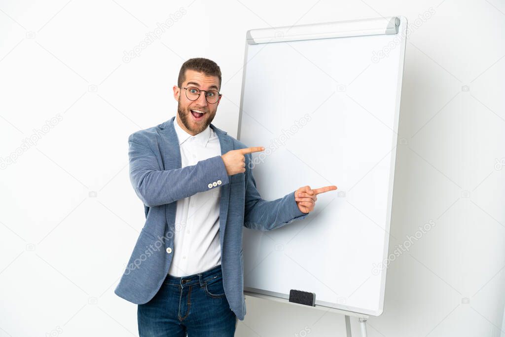 Young handsome caucasian man isolated on white background giving a presentation on white board and surprised while pointing side