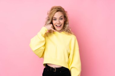 Pembe arka planda izole edilmiş svetşört giyen genç sarışın bir kadın telefon jesti yapıyor. Bana geri dönüş işareti ver.