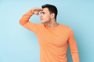 Beyaz tenli yakışıklı adam mavi arka planda izole edilmiş. Bir şeye bakmak için uzaklara bakıyor.