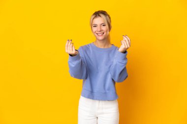 Sarı arka planda izole edilmiş genç Rus kadın para hareketi yapıyor.