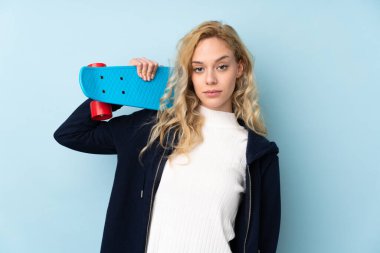 Genç sarışın kadın mavi arka planda tek başına paten kayıyor.