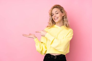 Pembe arka planda izole edilmiş eşofman üstü giyen genç sarışın kadın bir ilan vermek için avucunda hayali bir fotokopi makinesi tutuyor.