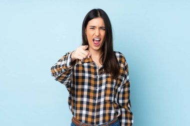 Mavi arka planda izole edilmiş genç beyaz kadın hayal kırıklığına uğramış ve ön tarafı işaret ediyor.