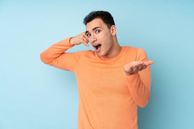 Beyaz tenli yakışıklı bir adam mavi arka planda izole edilmiş telefon jestleri yapıyor.