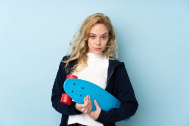 Genç sarışın kadın mavi arka planda tek başına paten kayıyor.