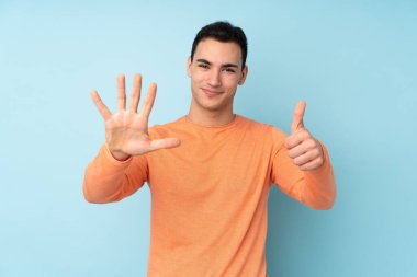 Beyaz tenli yakışıklı adam mavi arka planda izole edilmiş. Parmakları olan altı kişi saydım.
