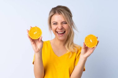 Sarışın kadın izole edilmiş mavi arka planda elinde bir portakal tutuyor.