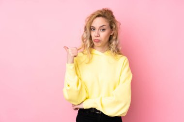 Pembe arka planda izole edilmiş sweatshirt giyen genç sarışın kadın mutsuzdu ve yan tarafı gösteriyordu.