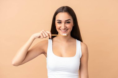 Beyaz tenli genç bir kadın bej arka planda izole edilmiş diş fırçası ve mutlu bir ifadeyle