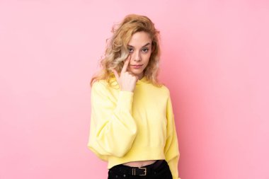 Pembe arka planda izole edilmiş sweatshirt giyen genç sarışın kadın bir şey gösteriyor.