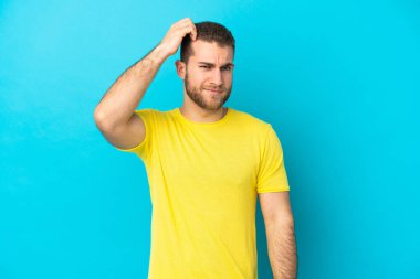 Genç, beyaz, mavi arka planda izole edilmiş, kafası kaşınırken kuşkuları olan bir adam.