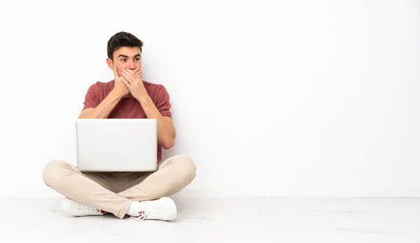 Nastolatek Siedzący Podłodze Laptopem Zasłaniającym Usta Patrzący Boku — Zdjęcie stockowe