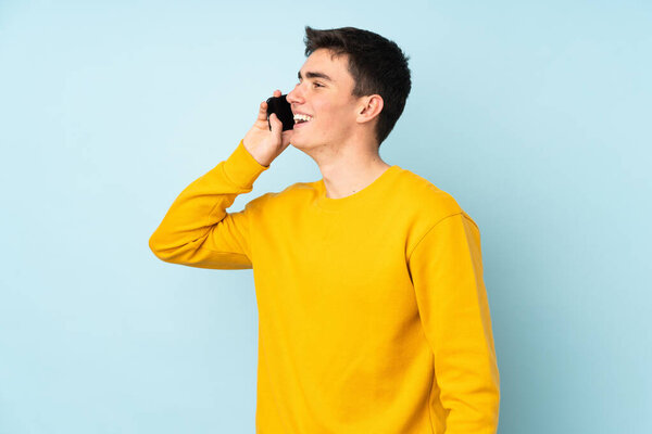 Teenager caucasian handsome man isolated on purple background keeping a conversation with the mobile phone