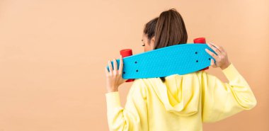 Kafkasyalı genç bir kadın pembe arka planda izole edilmiş ve arka planda kaykay yapıyor.