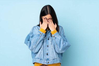 Kafkasyalı genç bir kadın mavi arka planda izole edilmiş, yorgun ve hasta bir ifadeyle.