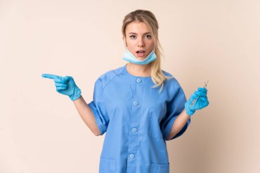 Dişçi kadın, elinde aletleri izole edilmiş arka planda tutuyor. Şaşırmış ve işaret ediyor.