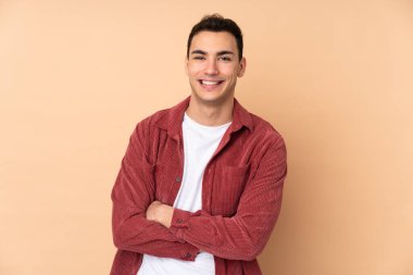 Beyaz tenli yakışıklı adam bej arka planda izole edilmiş ve kollarını ön cephede kavuşturuyor.