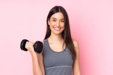 Pembe arka planda izole haldeyken halter kaldıran genç kadın çok gülümsüyor.