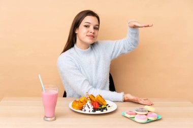 Bej arka planda izole edilmiş waffle yiyen genç kız reklam koymak için kopyalama alanı tutuyor