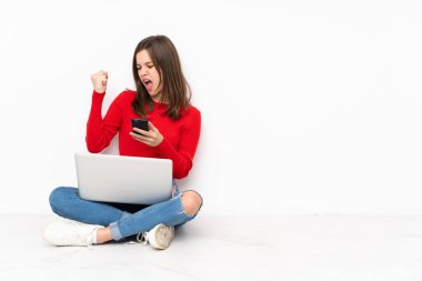 Bilgisayarla çalışan tenaager kız beyaz arka planda izole edilmiş ve telefon zafer pozisyonunda.