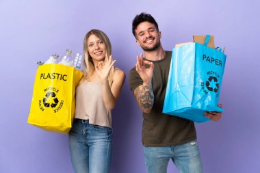 Mor arka planda izole edilmiş beyaz çift geri dönüşüm yaparken parmaklarında sorun olmadığını gösteriyor.