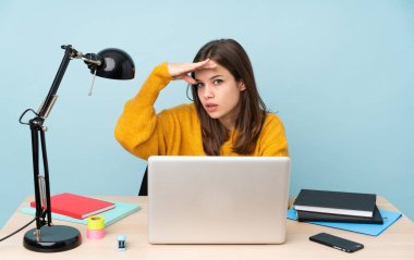 Öğrenci kız evinde çalışıyor. Mavi arka planda izole edilmiş. Bir şeye bakmak için uzaklara bakıyor.