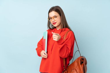 Mavi arka planda izole edilmiş kitapları tutan öğrenci kız seni işaret ediyor.