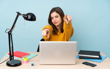 Evinde okuyan öğrenci kız mavi arka planda izole bir şekilde gülümserken seni işaret ediyor.