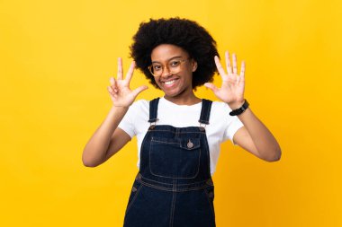 Sarı arka planda izole edilmiş genç Afrikalı Amerikalı kadın parmaklarıyla sekiz sayıyor.