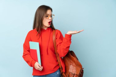 Mavi arka planda izole edilmiş kitapları tutan öğrenci kız avuç içinde sanal bir boşluğu tutuyor.