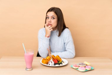 Bej arka planda izole edilmiş waffle yiyen genç kız gergin ve korkmuş.