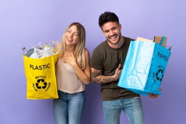 Mor arka planda izole edilmiş beyaz bir çift ellerini göğsüne koyup gülümsüyor.