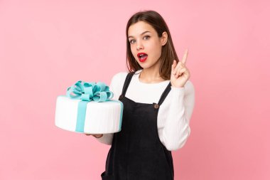 Pembe arka planda izole edilmiş büyük bir pastayı tutan kız parmağını kaldırırken çözümü bulmayı umuyor.