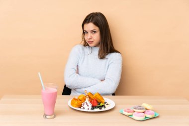 Bej arka planda izole edilmiş waffle yiyen genç kız üzgün