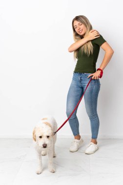 Köpeği gezdiren beyaz tenli genç bir kadın omuz ağrısı çektiği için beyaz arka planda izole edilmiş.